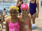 Two young girls in swim caps and one is wearing a pink swimming cap.