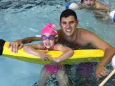 A man and girl in the pool with an inflatable raft.