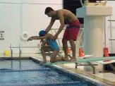 A man and boy in the pool jumping off of a diving board.
