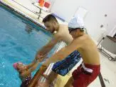 Two men in a pool with one holding onto the side of his head.