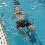 A man swimming in the pool with his arms out.